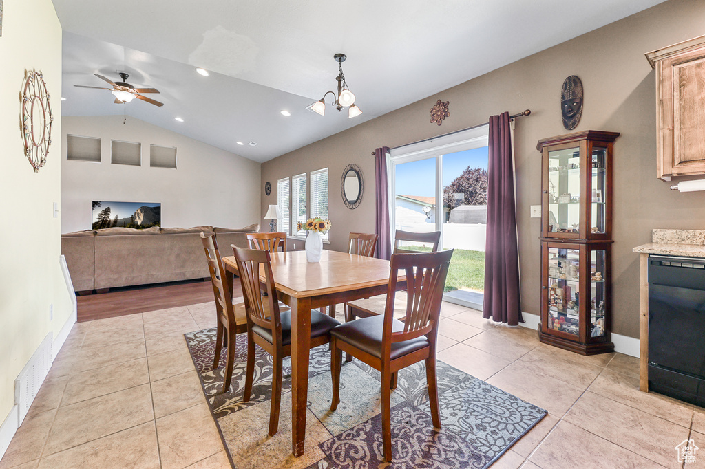 Tiled dining room with a healthy amount of sunlight, ceiling fan with notable chandelier, and lofted ceiling