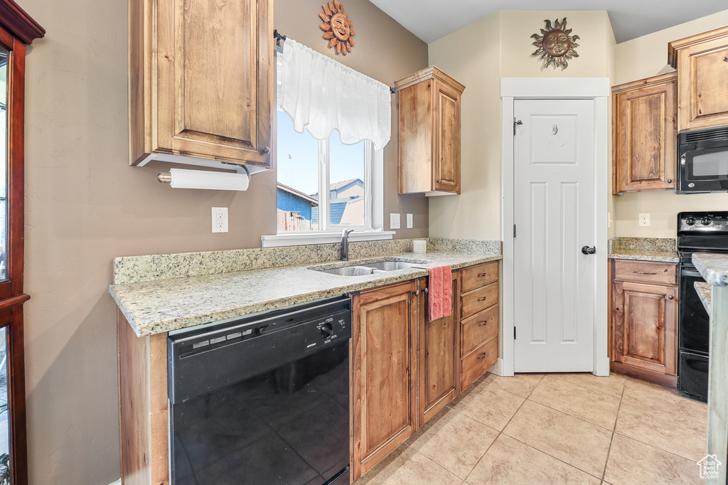 Kitchen featuring light tile patterned flooring, sink, light stone countertops, and black appliances