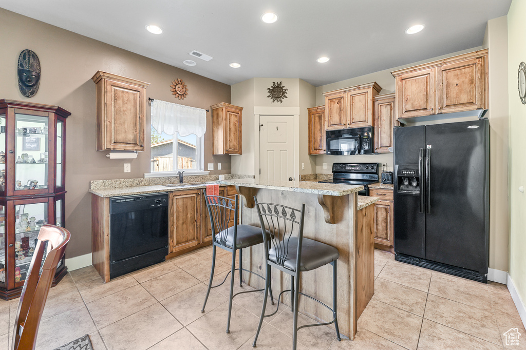 Kitchen featuring a kitchen breakfast bar, black appliances, a kitchen island, and light tile patterned floors