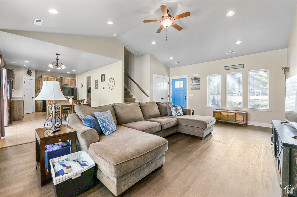 Living room featuring light hardwood / wood-style flooring, ceiling fan with notable chandelier, and vaulted ceiling