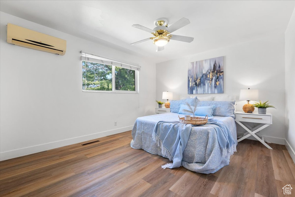 Bedroom featuring ceiling fan, a wall mounted air conditioner, and hardwood / wood-style flooring