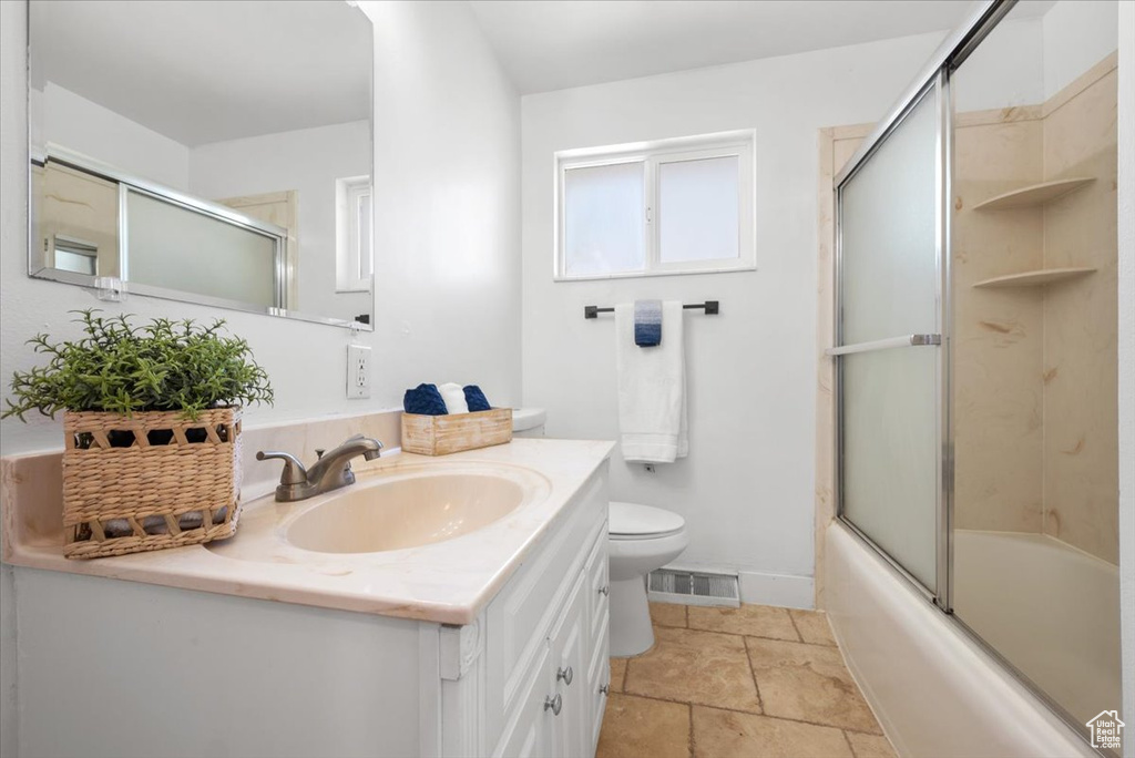 Full bathroom featuring combined bath / shower with glass door, vanity, toilet, and tile patterned flooring