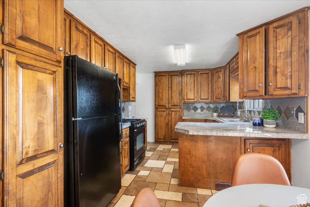 Kitchen with tasteful backsplash, light tile patterned flooring, black appliances, sink, and kitchen peninsula