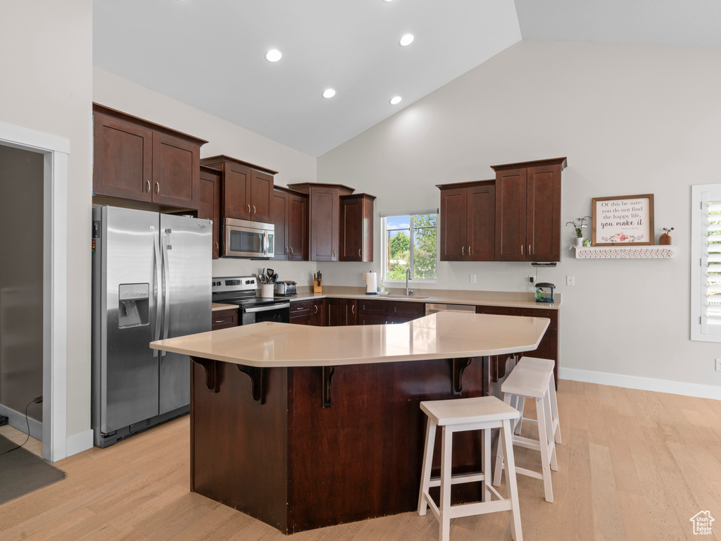 Kitchen with high vaulted ceiling, a spacious island, stainless steel appliances, and light hardwood / wood-style floors