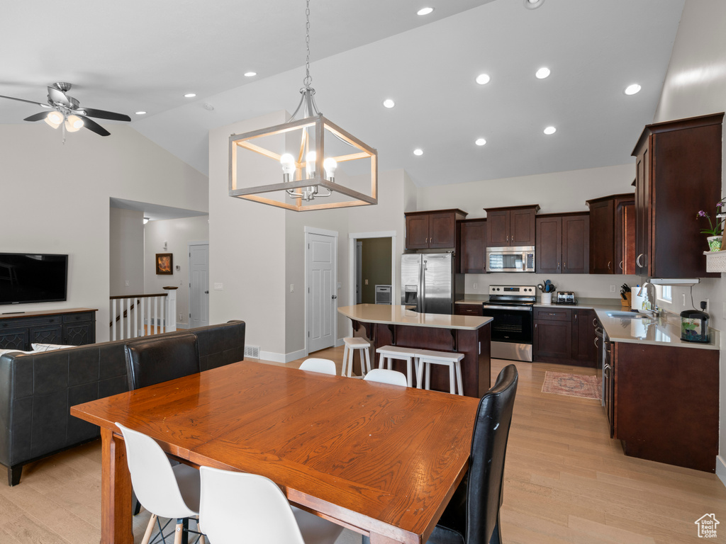 Dining room featuring light hardwood / wood-style floors, sink, ceiling fan with notable chandelier, and high vaulted ceiling