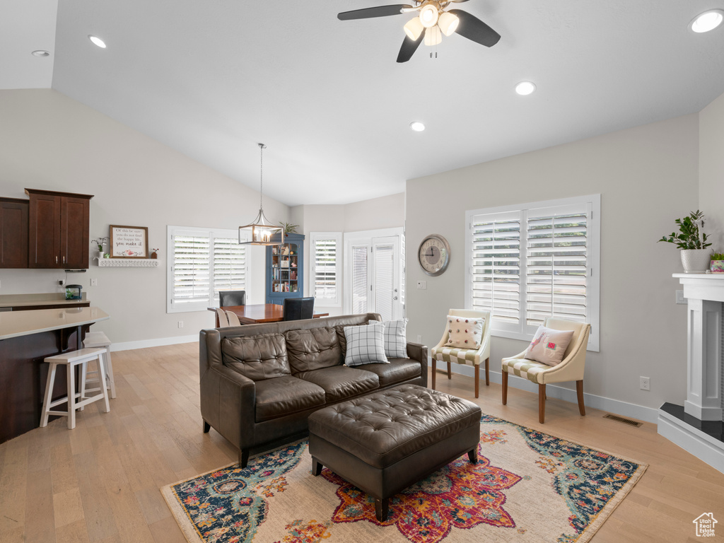 Living room featuring ceiling fan with notable chandelier, lofted ceiling, and light hardwood / wood-style floors