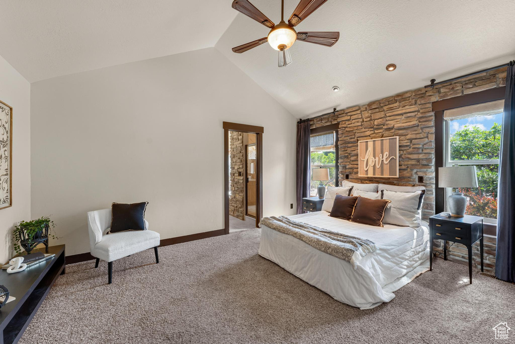 Carpeted bedroom featuring multiple windows, ensuite bath, ceiling fan, and high vaulted ceiling