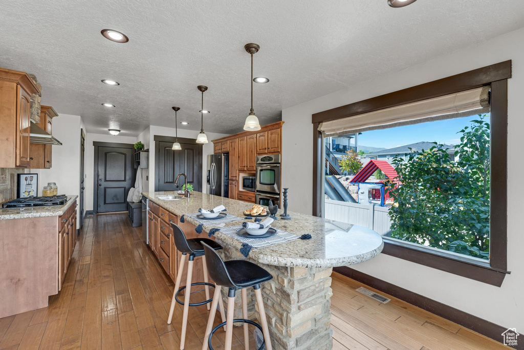 Kitchen featuring light hardwood / wood-style flooring, appliances with stainless steel finishes, sink, and an island with sink