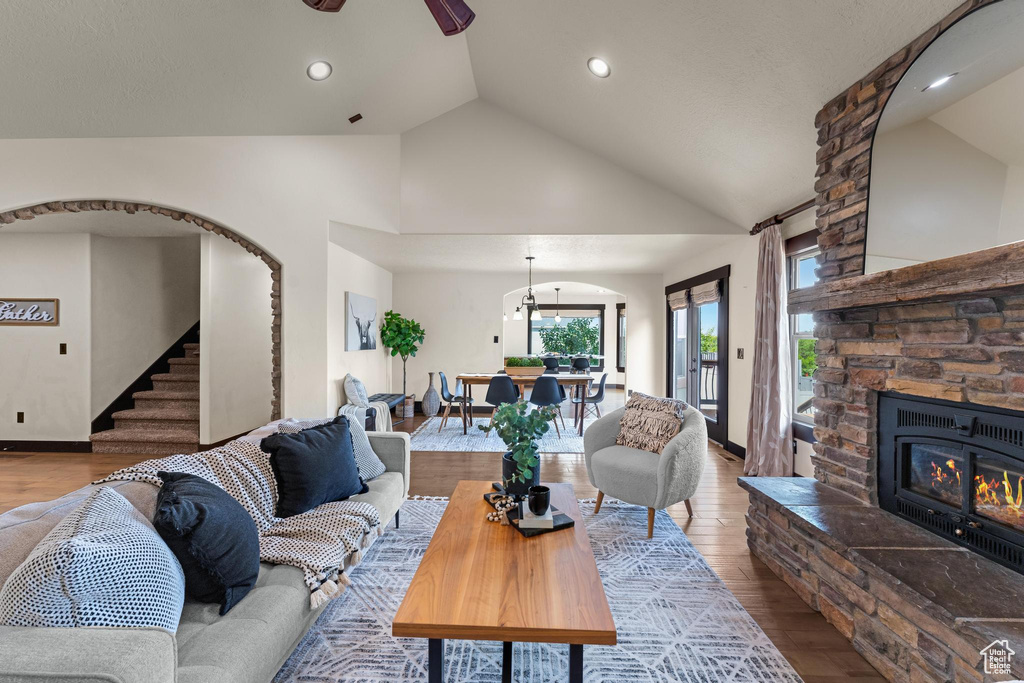 Living room featuring a stone fireplace, hardwood / wood-style floors, high vaulted ceiling, and ceiling fan