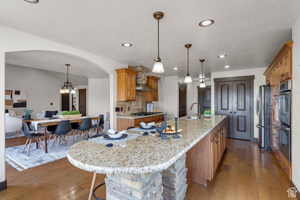 Kitchen with backsplash, an island with sink, stainless steel appliances, hardwood / wood-style flooring, and sink