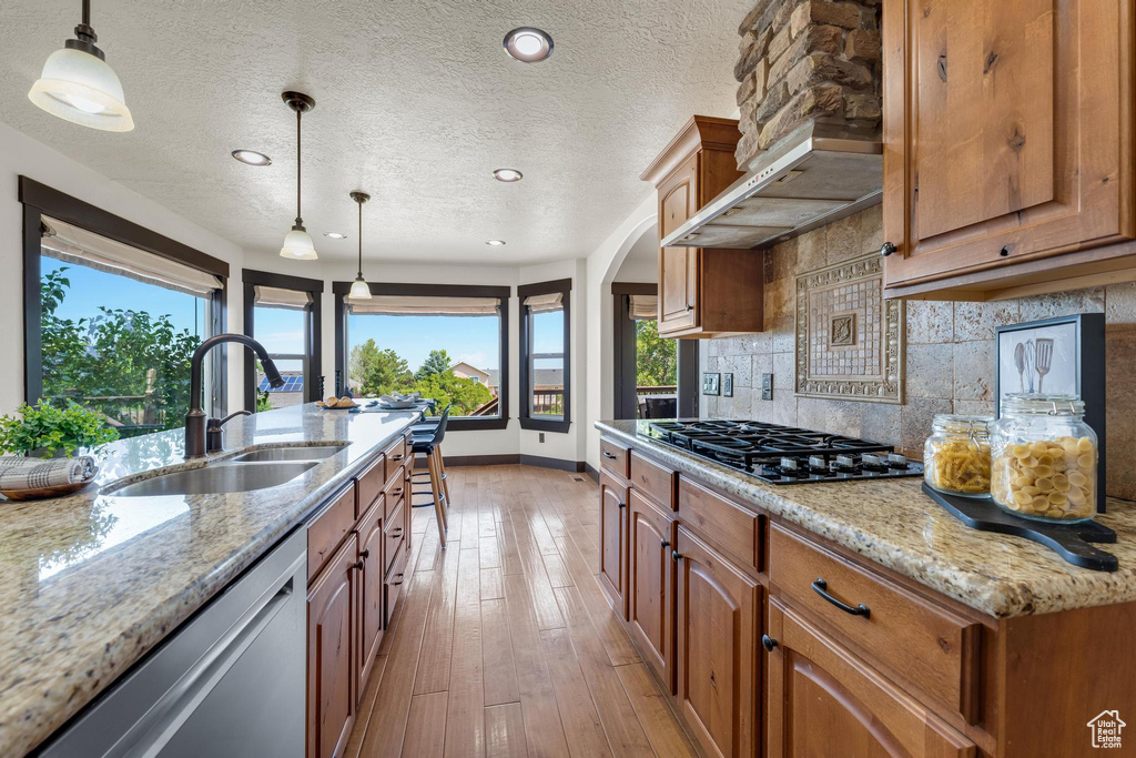 Kitchen with tasteful backsplash, wall chimney range hood, light hardwood / wood-style floors, decorative light fixtures, and sink