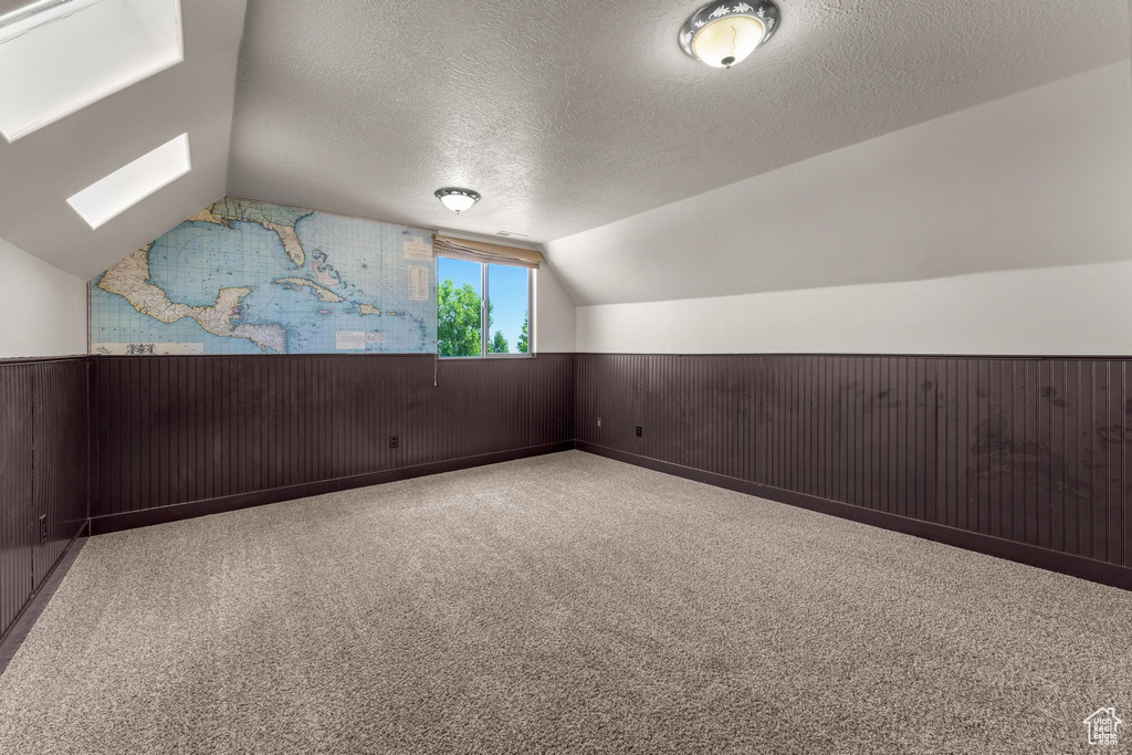 Bonus room featuring a textured ceiling, vaulted ceiling with skylight, and light colored carpet