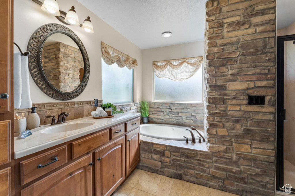 Bathroom with a relaxing tiled tub, tile patterned floors, vanity, and a textured ceiling