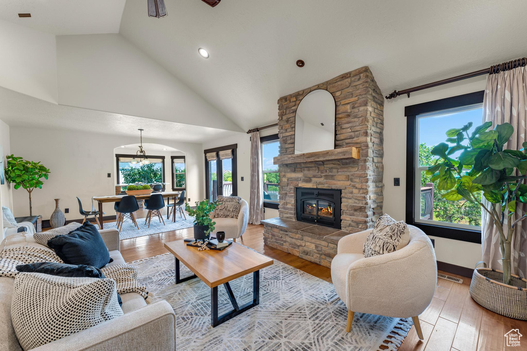 Living room with light hardwood / wood-style floors, high vaulted ceiling, a stone fireplace, and plenty of natural light