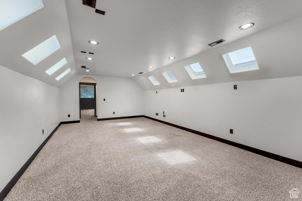 Bonus room with carpet flooring, a textured ceiling, and vaulted ceiling with skylight