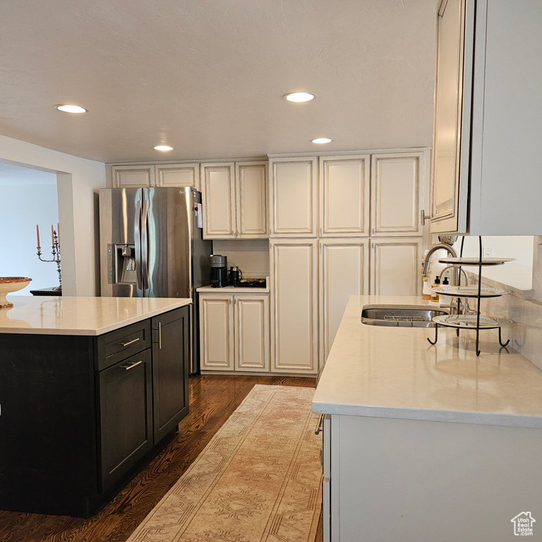 Kitchen featuring cream cabinets, hardwood / wood-style flooring, stainless steel fridge with ice dispenser, sink, and light stone countertops