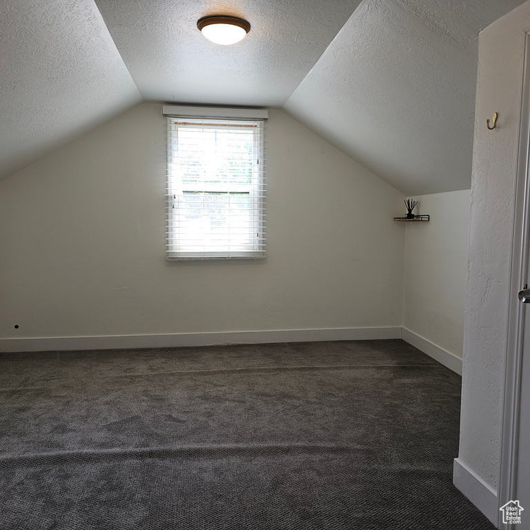 Bonus room featuring dark carpet, a textured ceiling, and vaulted ceiling