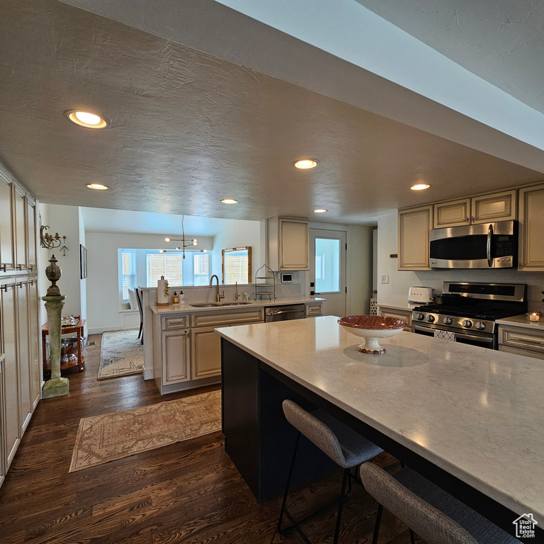 Kitchen featuring stainless steel appliances, sink, dark hardwood / wood-style floors, kitchen peninsula, and a kitchen breakfast bar