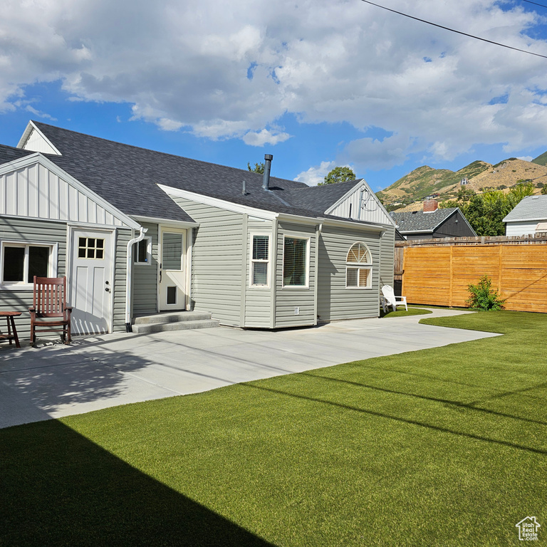 Rear view of property featuring a mountain view, a lawn, and a patio