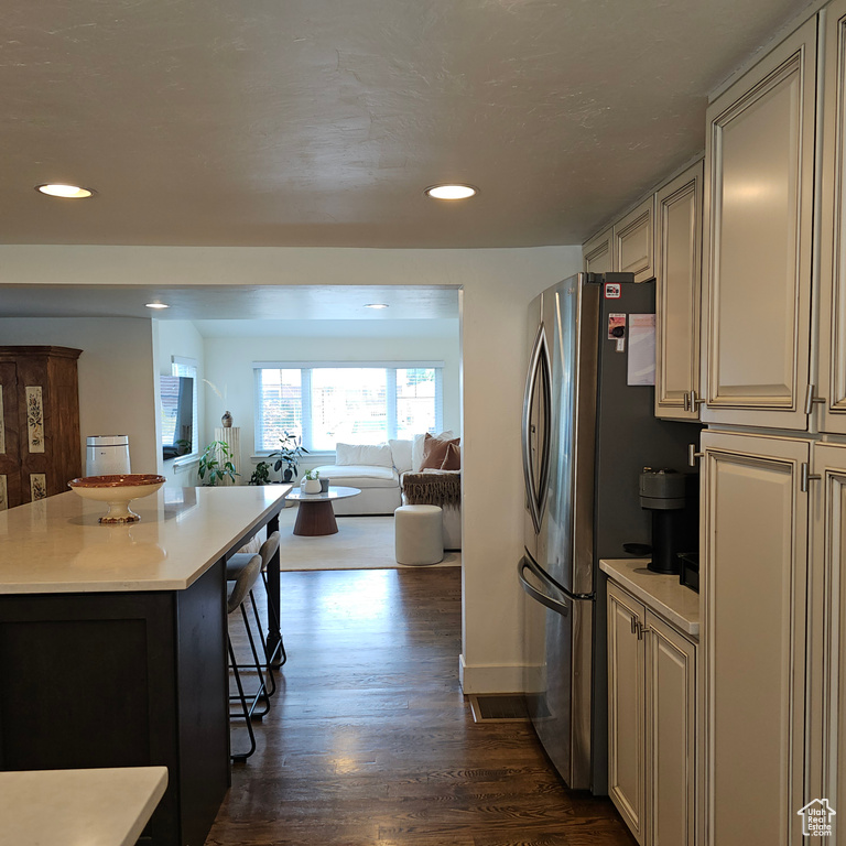 Kitchen with cream cabinets, dark hardwood / wood-style flooring, and stainless steel refrigerator