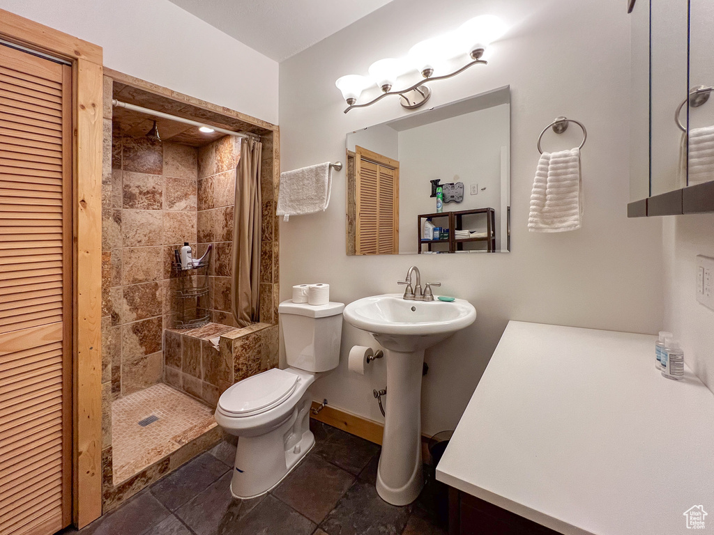 Bathroom featuring tiled shower, toilet, tile patterned flooring, and sink