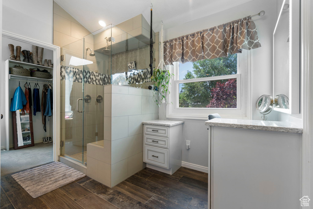 Bathroom with a shower with shower door, vanity, wood-type flooring, and vaulted ceiling