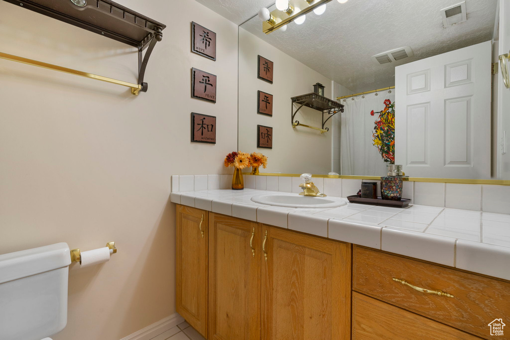 Bathroom with vanity, toilet, a textured ceiling, and tile patterned flooring