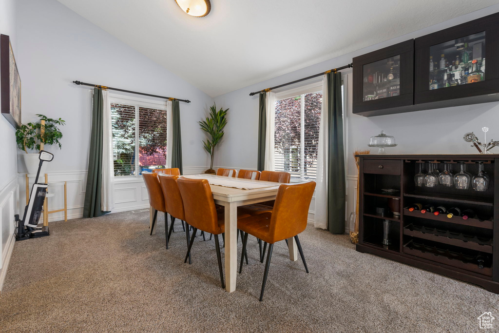 Dining room with carpet floors, bar, and vaulted ceiling