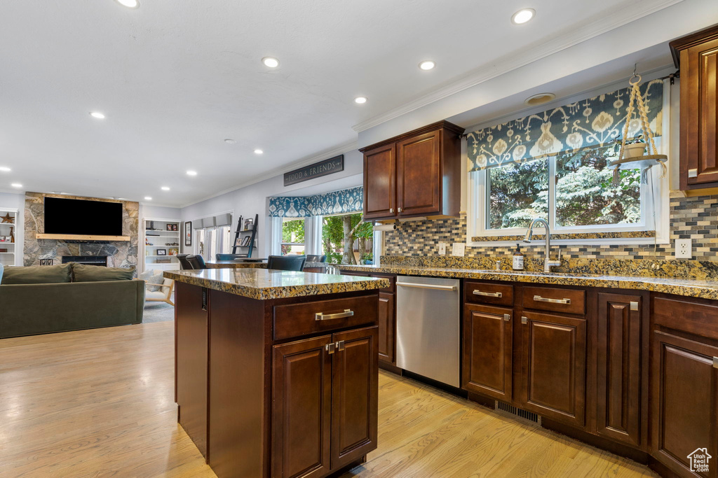 Kitchen featuring light hardwood / wood-style flooring, backsplash, dishwasher, a stone fireplace, and sink