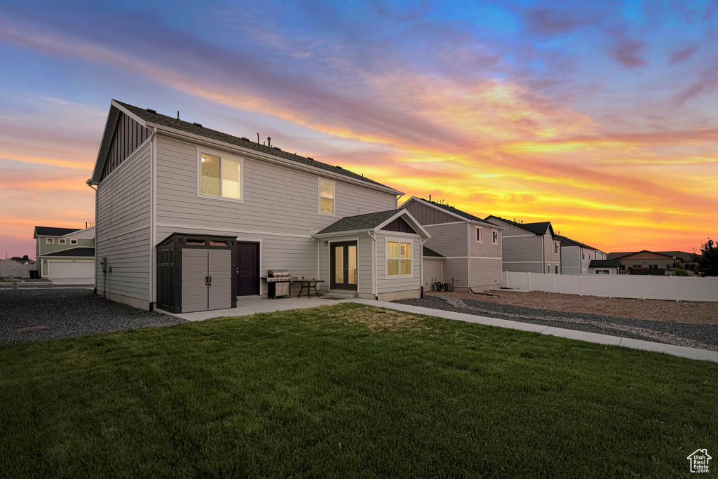 Back house at dusk featuring a garage and a lawn