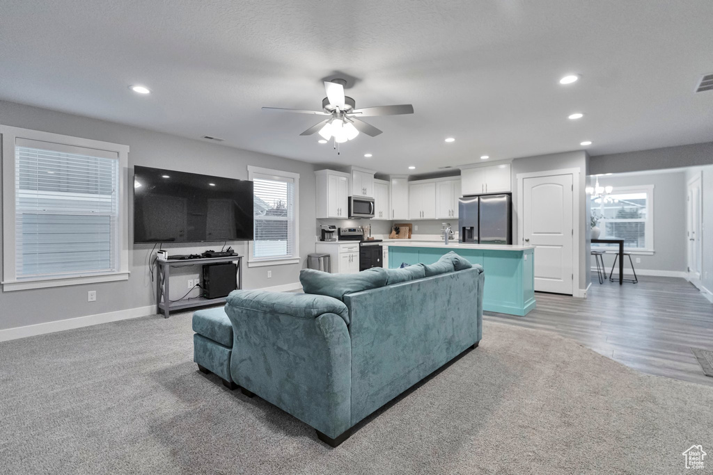 Living room featuring ceiling fan with notable chandelier and light carpet