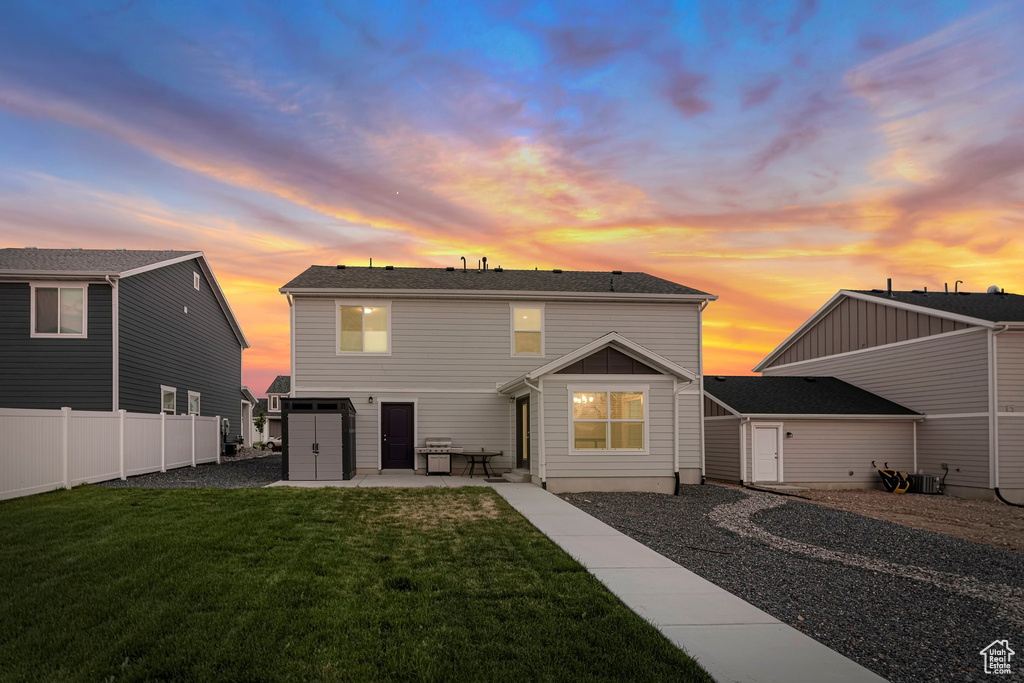 Back house at dusk with central AC unit, a patio area, and a yard