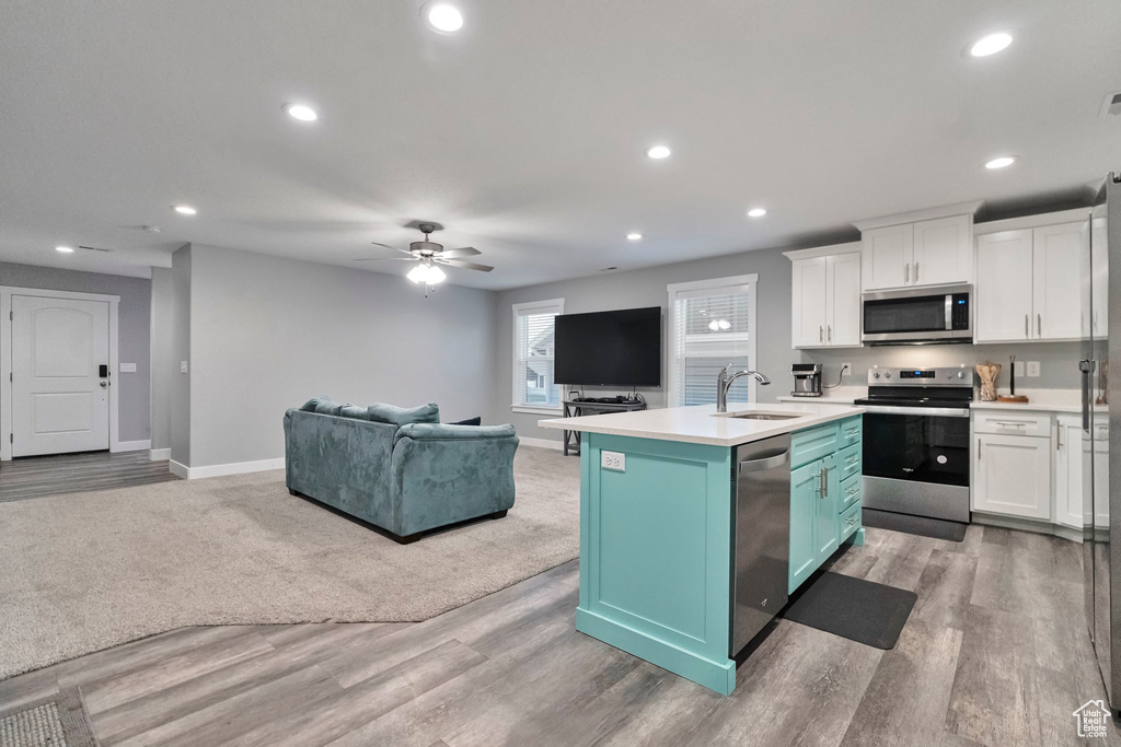 Kitchen with white cabinetry, appliances with stainless steel finishes, ceiling fan, and light colored carpet