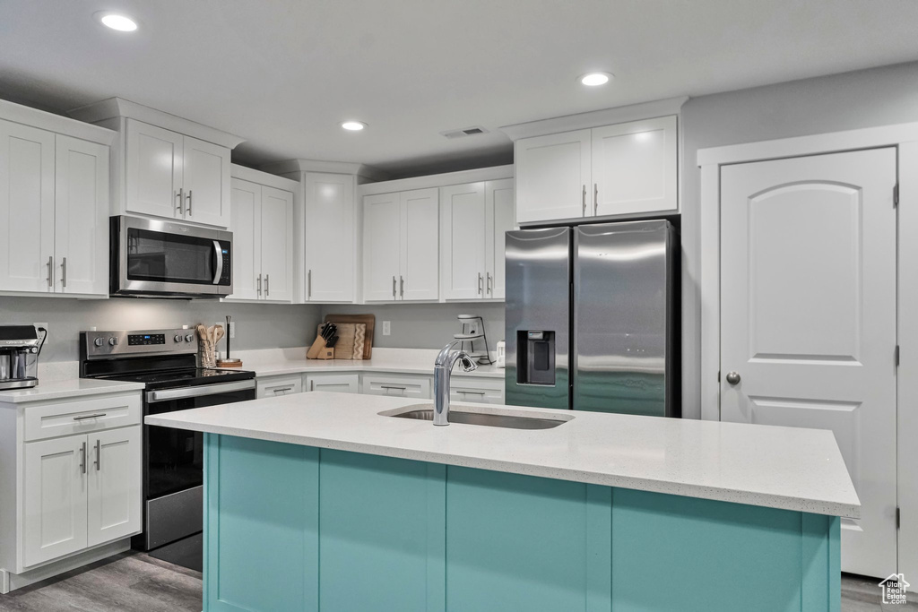 Kitchen with white cabinets, hardwood / wood-style flooring, appliances with stainless steel finishes, and sink