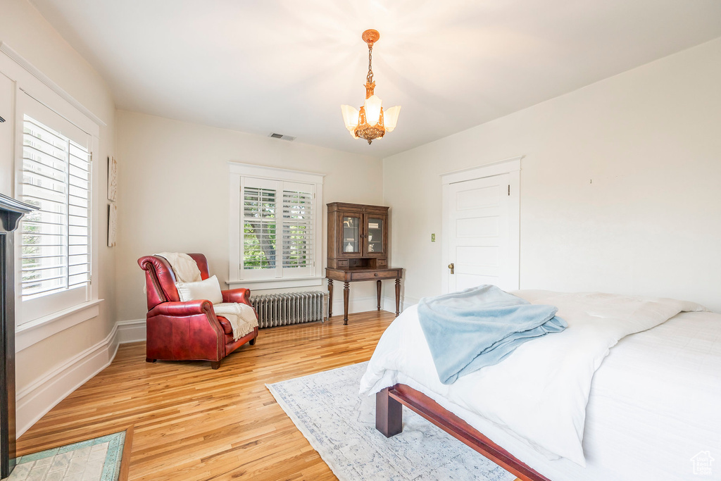 Bedroom with light hardwood / wood-style floors, radiator heating unit, multiple windows, and a notable chandelier