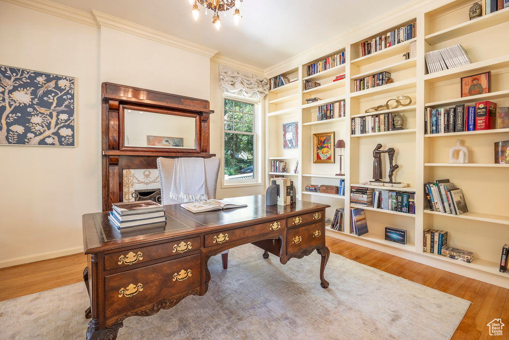 Home office featuring built in shelves, wood-type flooring, and ornamental molding