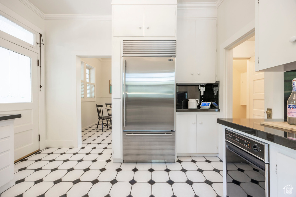 Kitchen featuring white cabinets, light tile patterned flooring, stainless steel built in refrigerator, and black oven