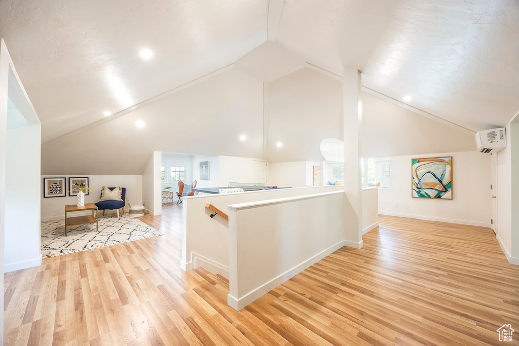 Interior space with light hardwood / wood-style flooring, a wall unit AC, and high vaulted ceiling