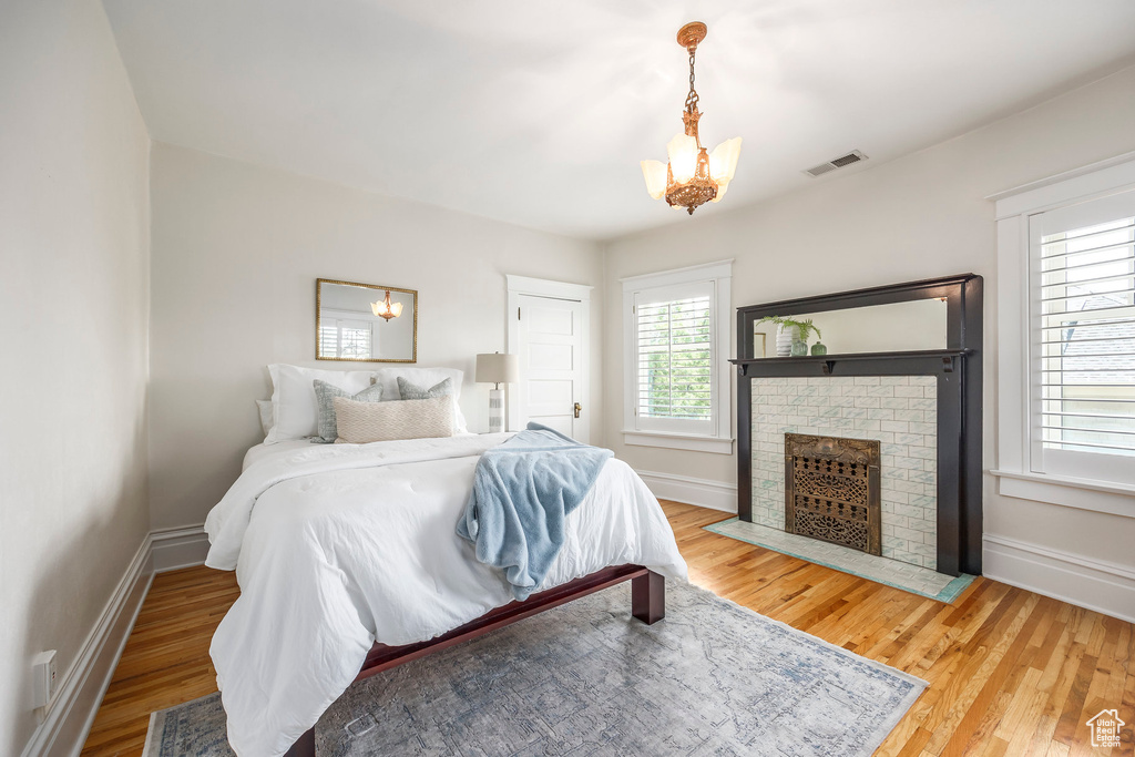 Bedroom with a brick fireplace, a notable chandelier, and hardwood / wood-style floors