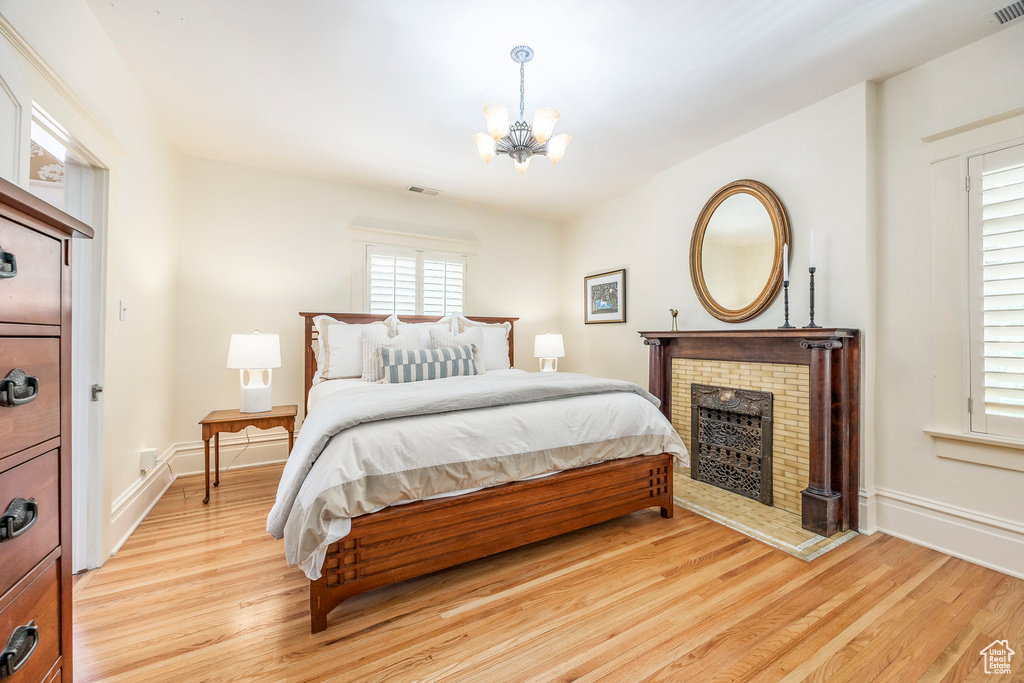 Bedroom with a brick fireplace, a notable chandelier, and light hardwood / wood-style floors