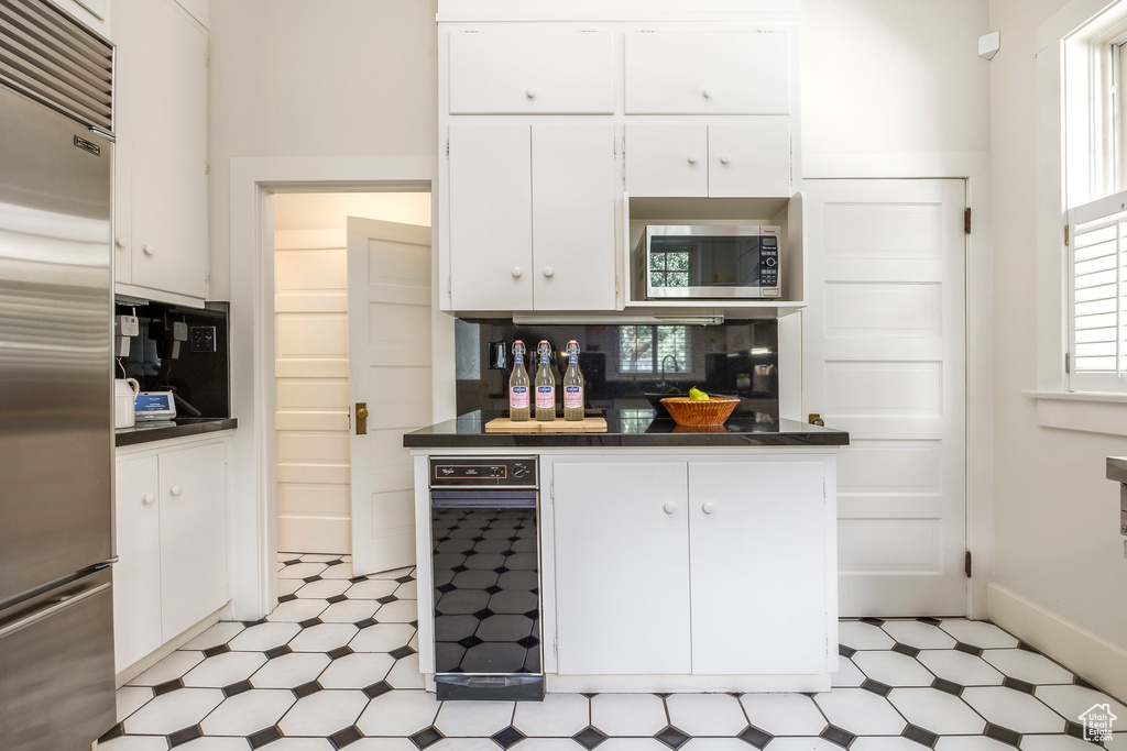 Kitchen with built in appliances, decorative backsplash, white cabinets, and light tile patterned floors