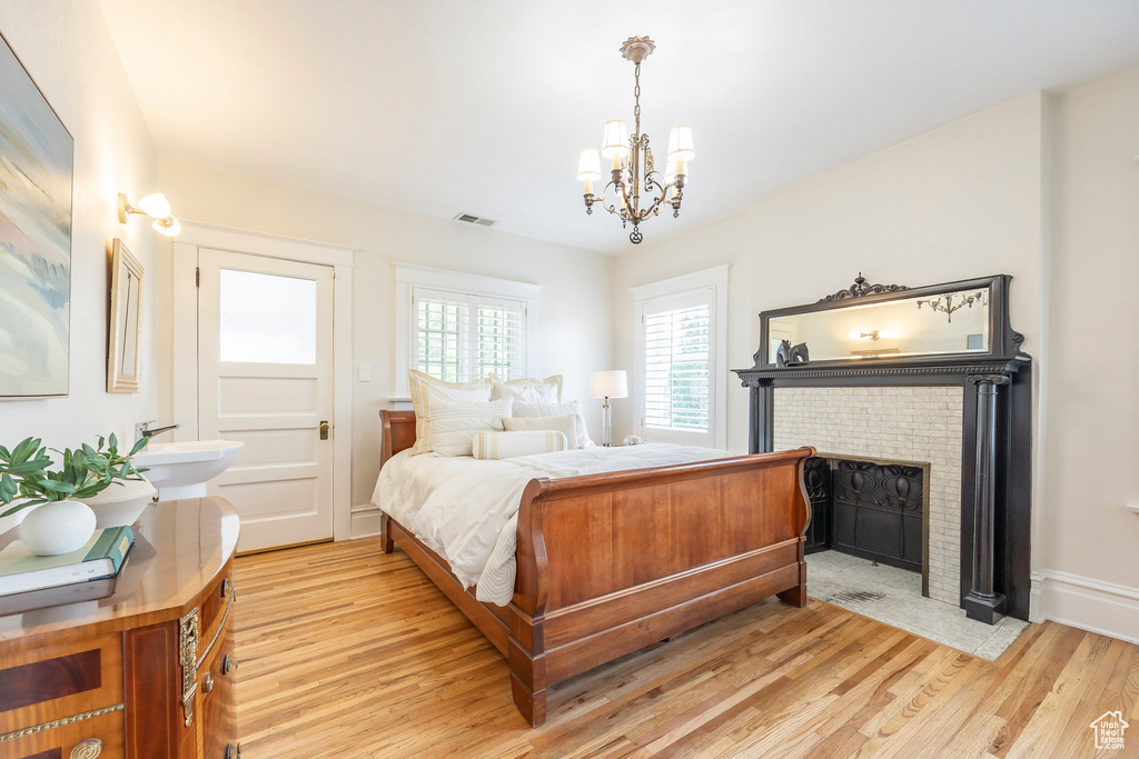 Bedroom featuring a fireplace, a notable chandelier, and light hardwood / wood-style floors