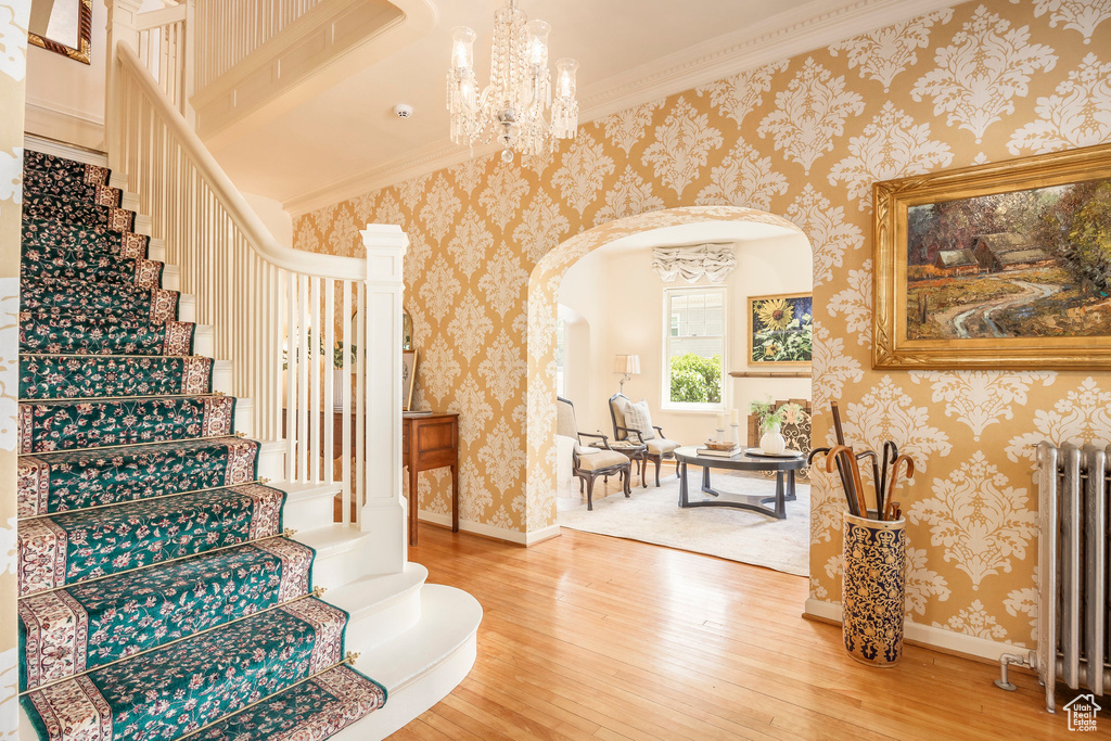 Stairs featuring wood-type flooring, radiator, crown molding, and an inviting chandelier