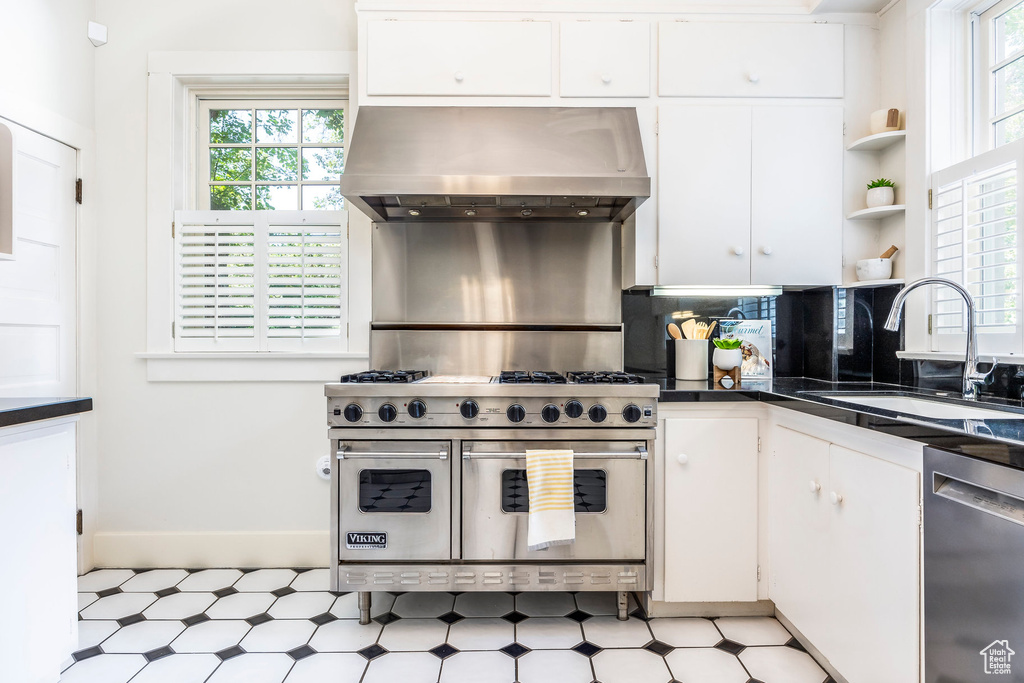 Kitchen with sink, appliances with stainless steel finishes, light tile patterned floors, and wall chimney range hood