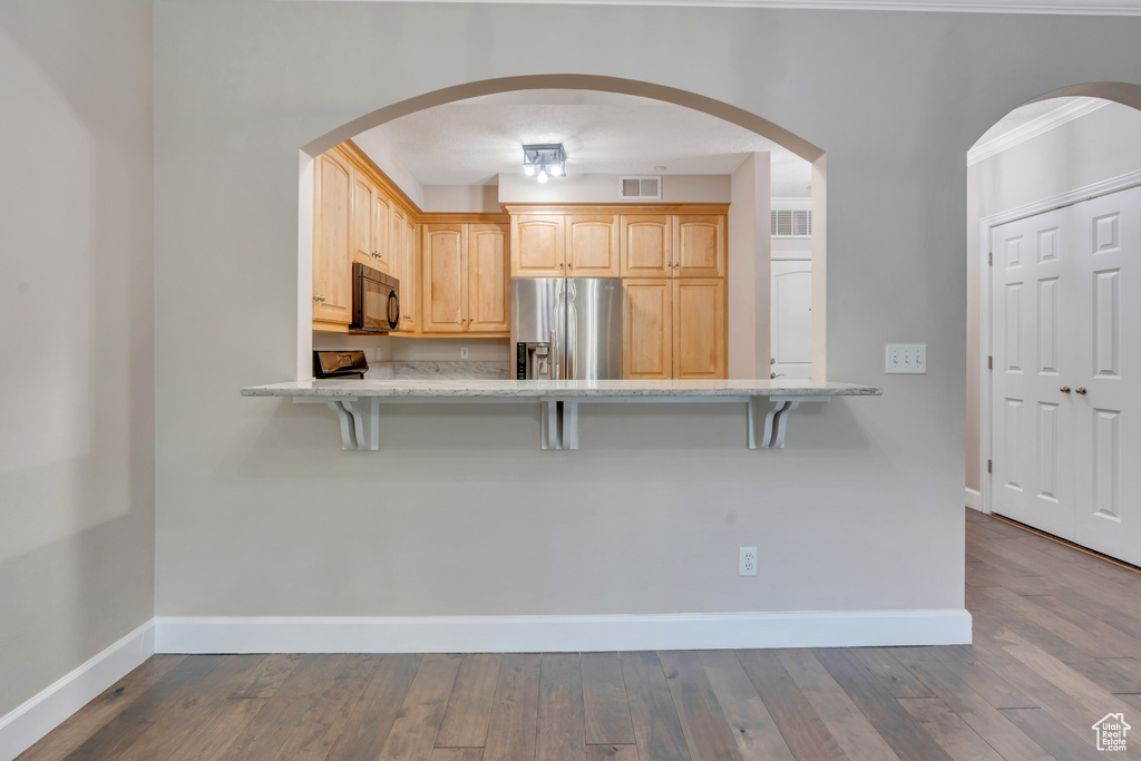 Kitchen with a kitchen bar, light brown cabinetry, wood-type flooring, and stainless steel refrigerator with ice dispenser