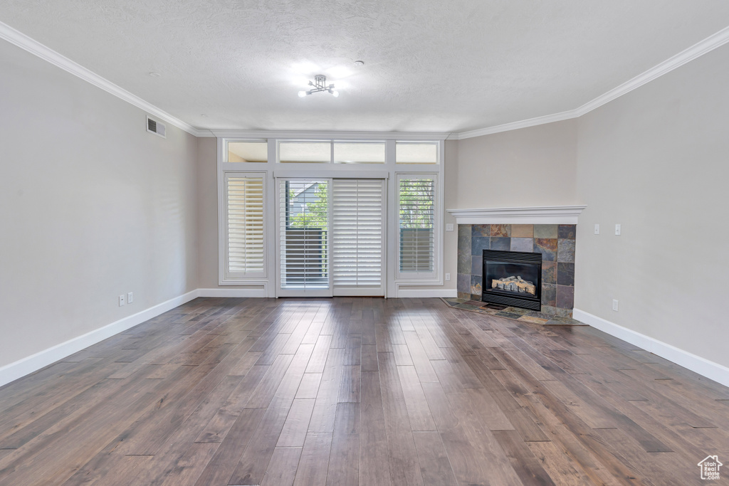 Unfurnished living room featuring a tiled fireplace, dark hardwood / wood-style floors, crown molding, and a textured ceiling