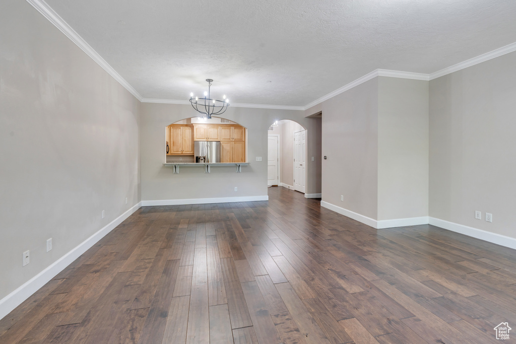 Unfurnished living room featuring crown molding, dark hardwood / wood-style flooring, a chandelier, and a textured ceiling