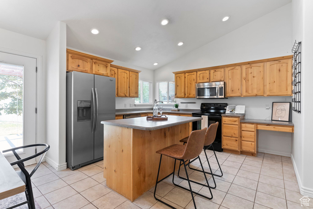 Kitchen featuring a breakfast bar area, stainless steel appliances, light tile patterned floors, lofted ceiling, and a center island