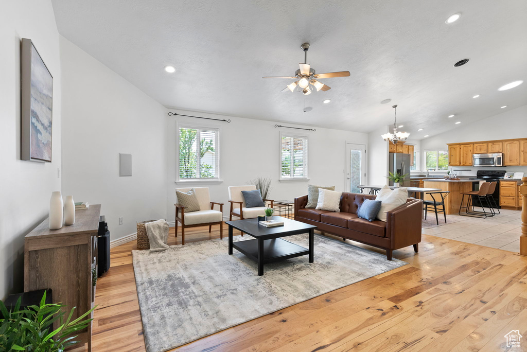 Living room with lofted ceiling, ceiling fan with notable chandelier, and light wood-type flooring