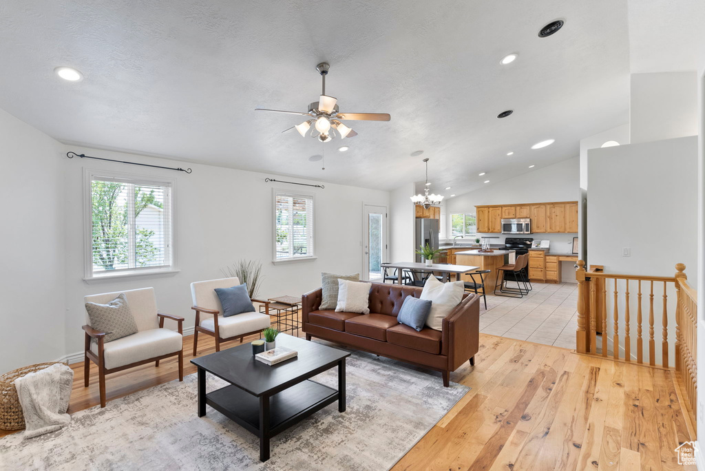 Living room with high vaulted ceiling, light wood-type flooring, and ceiling fan with notable chandelier